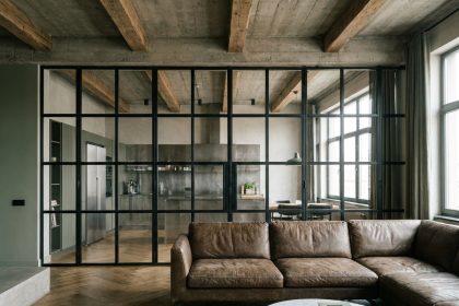 Verrière industrielle en acier noir séparant le séjour de la cuisine dans un appartement au style loft avec parquet en chêne et plafond en béton